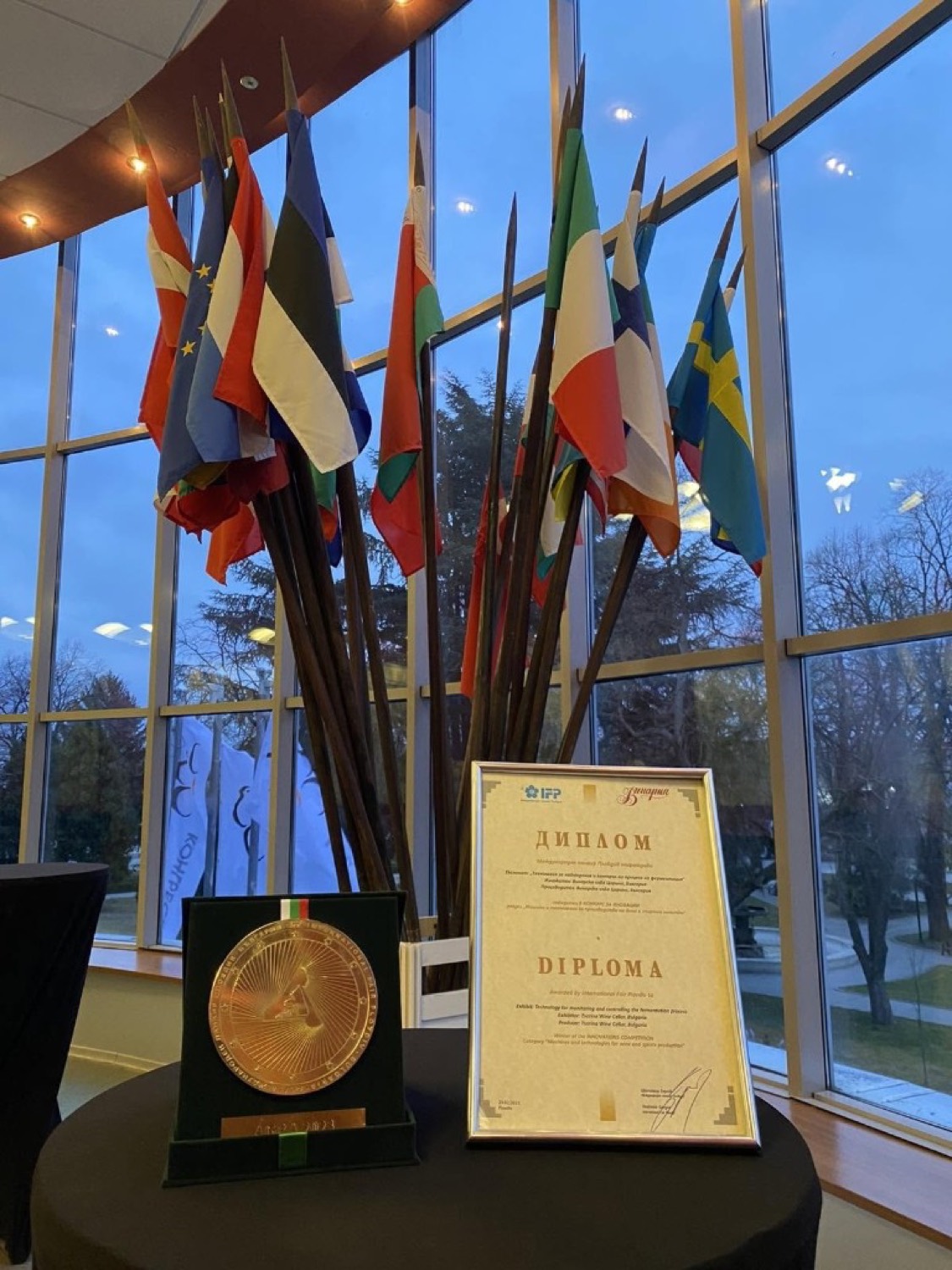 AGRA 2023 gold medal and framed bilingual diploma on a table, international flags behind