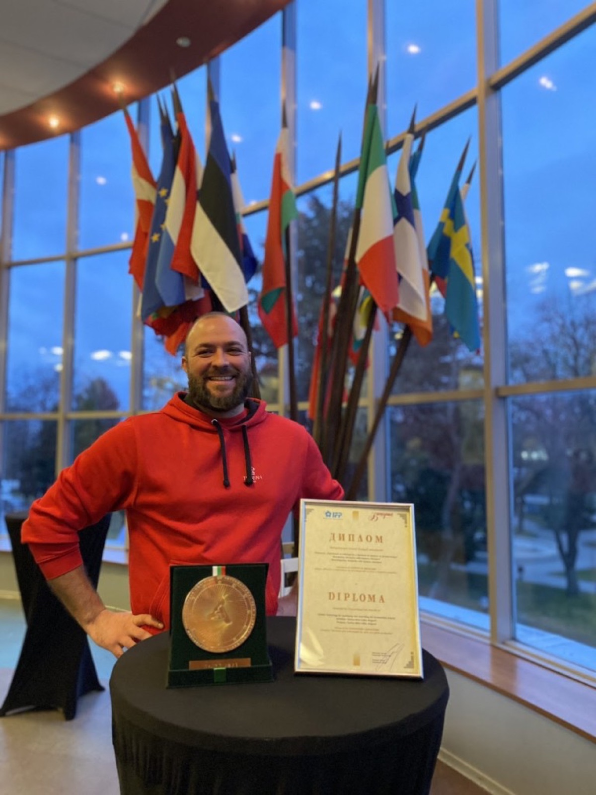 Founder posing with the AGRA 2023 gold medal and framed diploma, international flags behind
