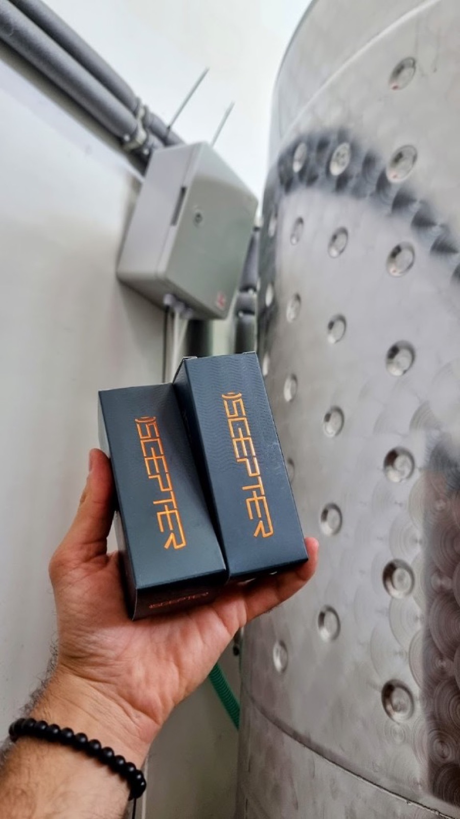 Hand holding two boxed SCEPTER devices beside a stainless steel tank with a mounted control box
